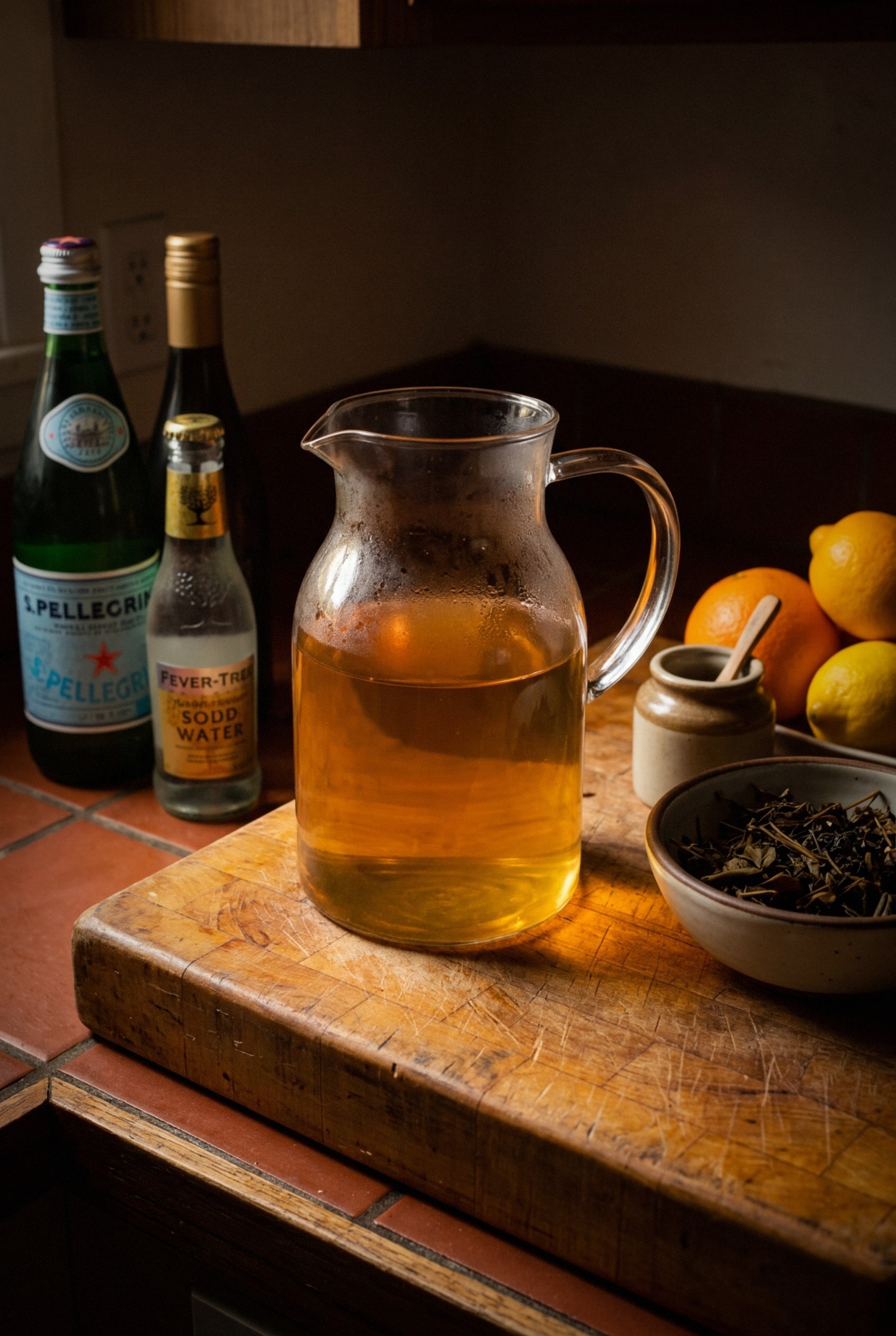 Hands straining cold-brewed adaptogenic stress relief tea through cheesecloth into glass pitcher, showing golden-amber liquid and spent herbs