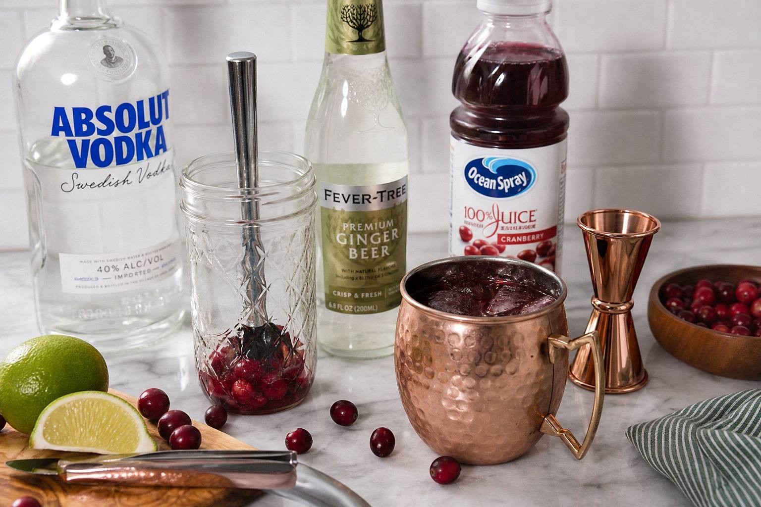 measured ingredients for cranberry moscow mule including ginger beer, cranberry juice, rum, lime, ice, and cranberries