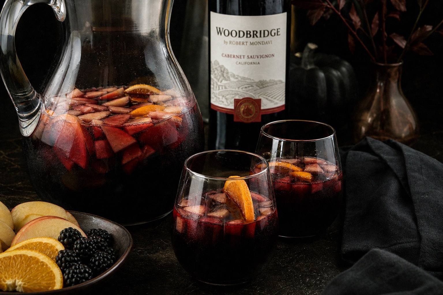 unmixed ingredients for halloween sangria including fresh blackberries, raspberries, black grapes, chopped apple, and bottles of wine and spirits