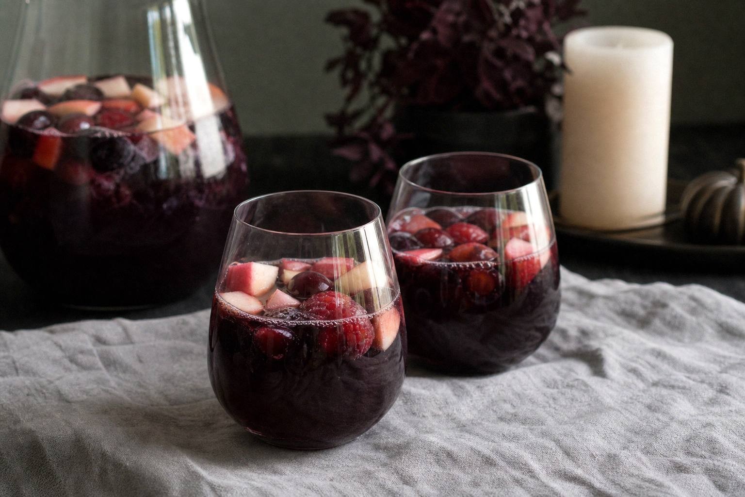 two finished servings of halloween sangria styled on a table with ice and fruit garnish in clear glasses