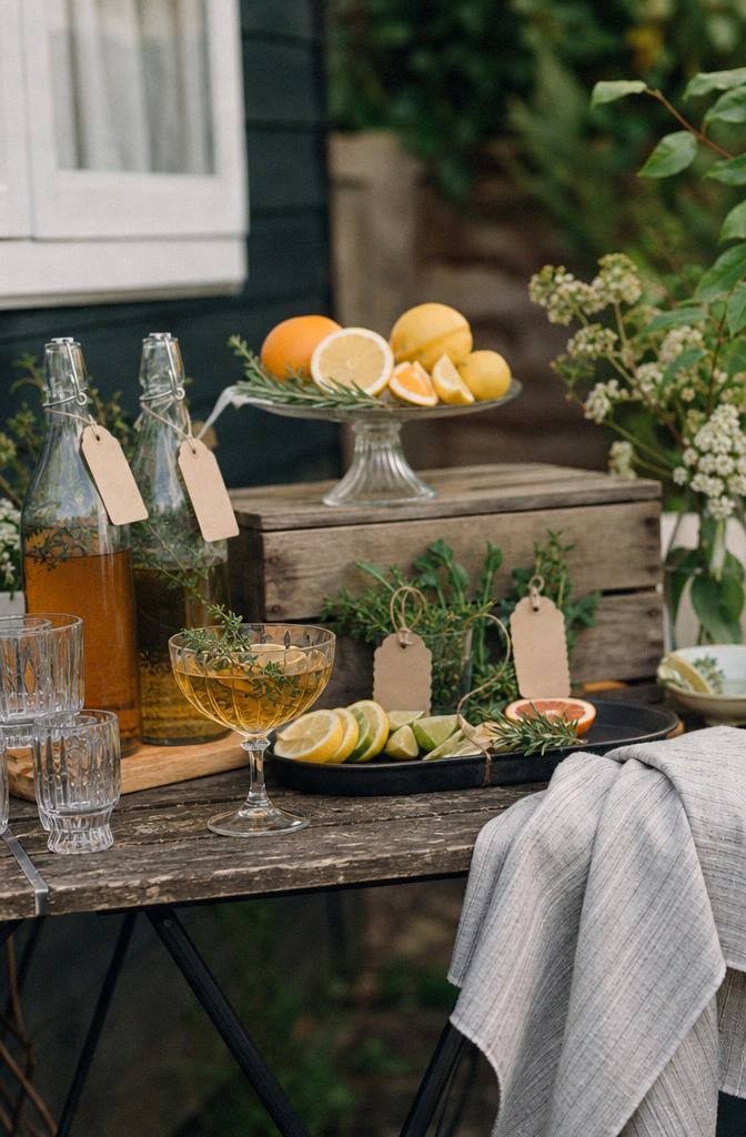 close-up of folding table drink bar with vintage glasses pitcher citrus herbs garnish tray and handwritten labels